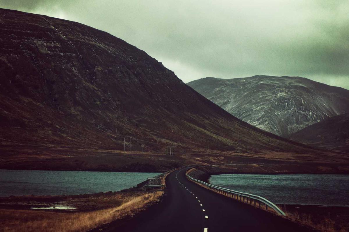 Winding road through dramatic mountains and lakes under an overcast sky, showcasing Iceland's rugged landscape.