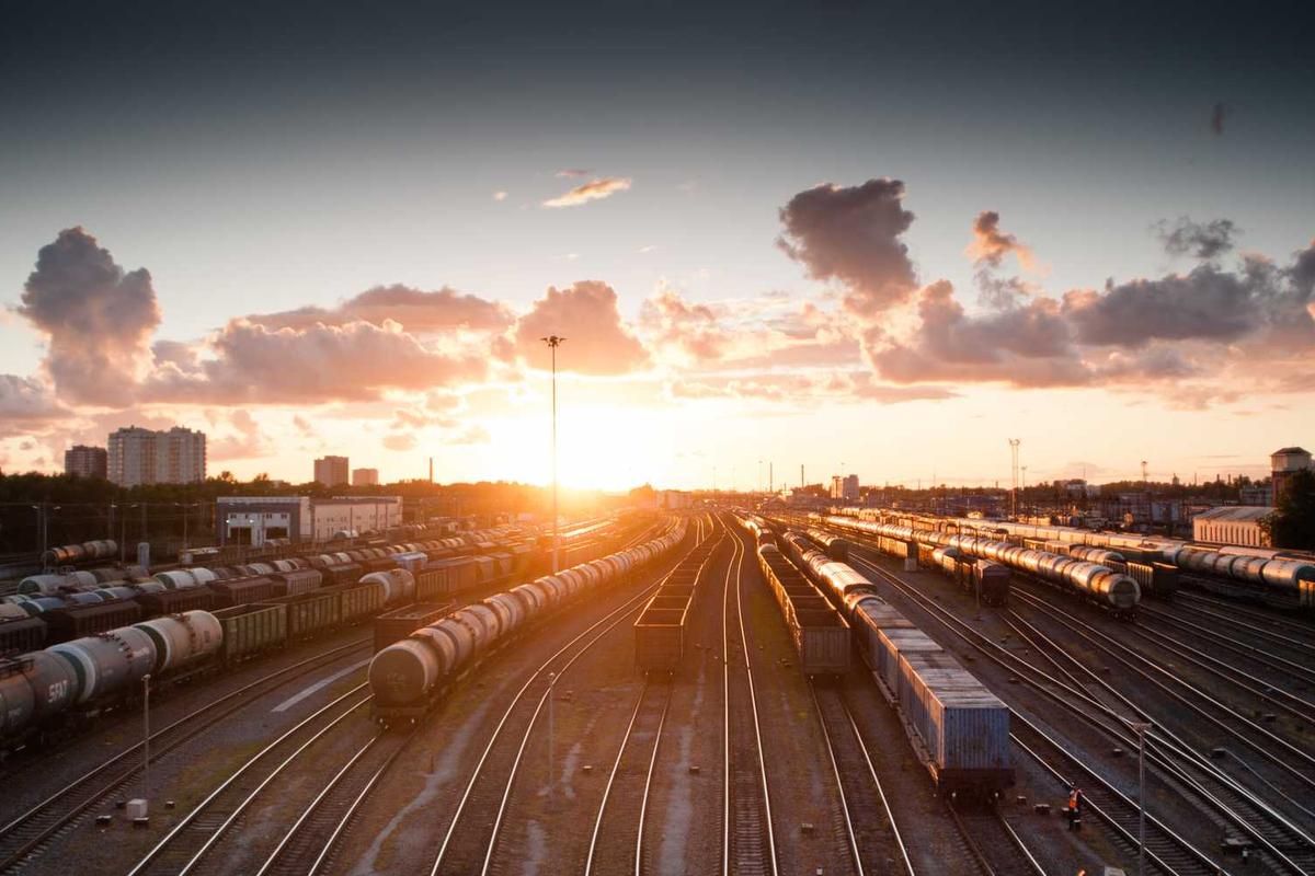 Sunset over a freight train yard, showcasing tracks and cargo cars against a colorful sky.