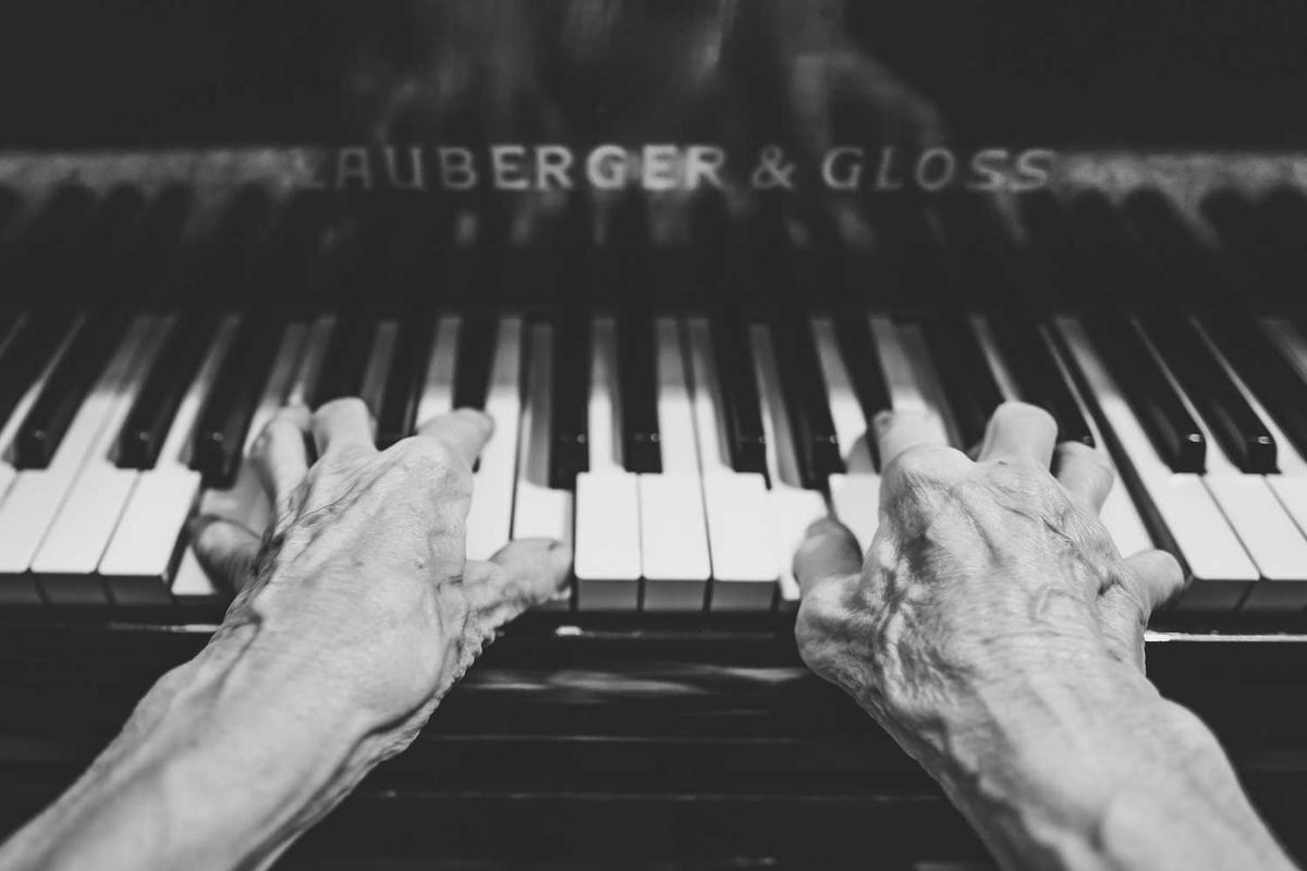 Close-up of aged hands playing piano keys, showcasing artistry and emotion in black and white.
