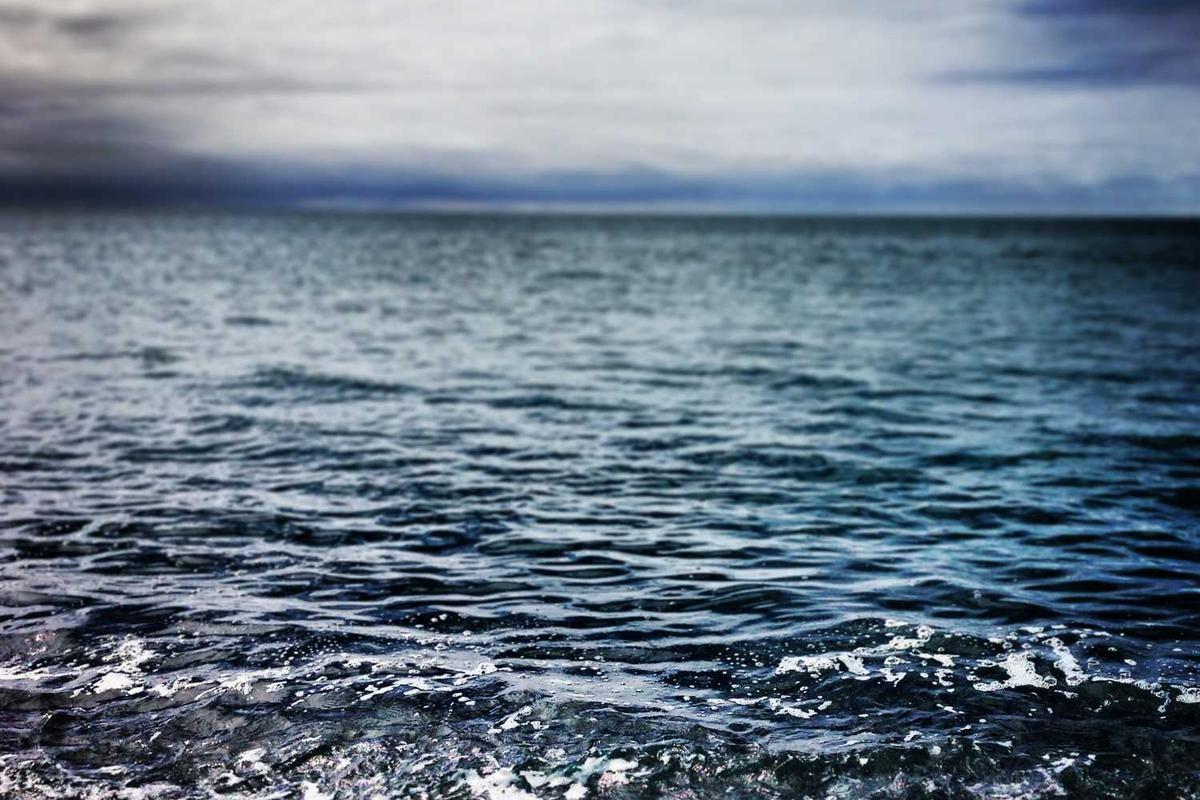 Gentle waves ripple on a serene ocean under a cloudy sky, creating a tranquil coastal atmosphere.