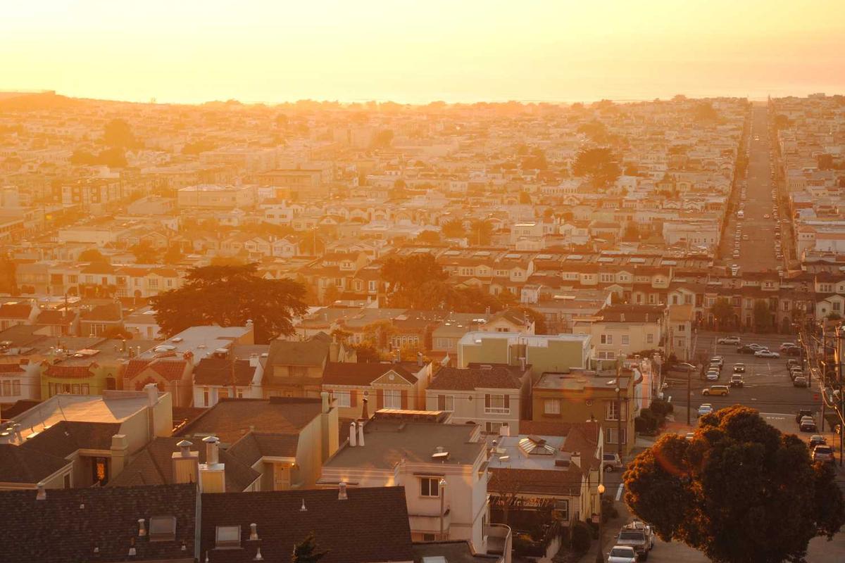Golden sunset view over a densely packed city landscape with rows of houses and a long, straight road.