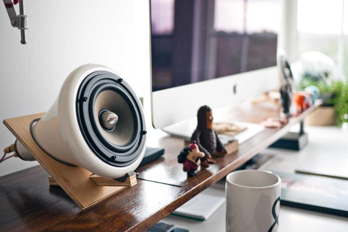 Modern desk setup featuring a stylish speaker, toys, and a coffee mug next to a computer monitor.