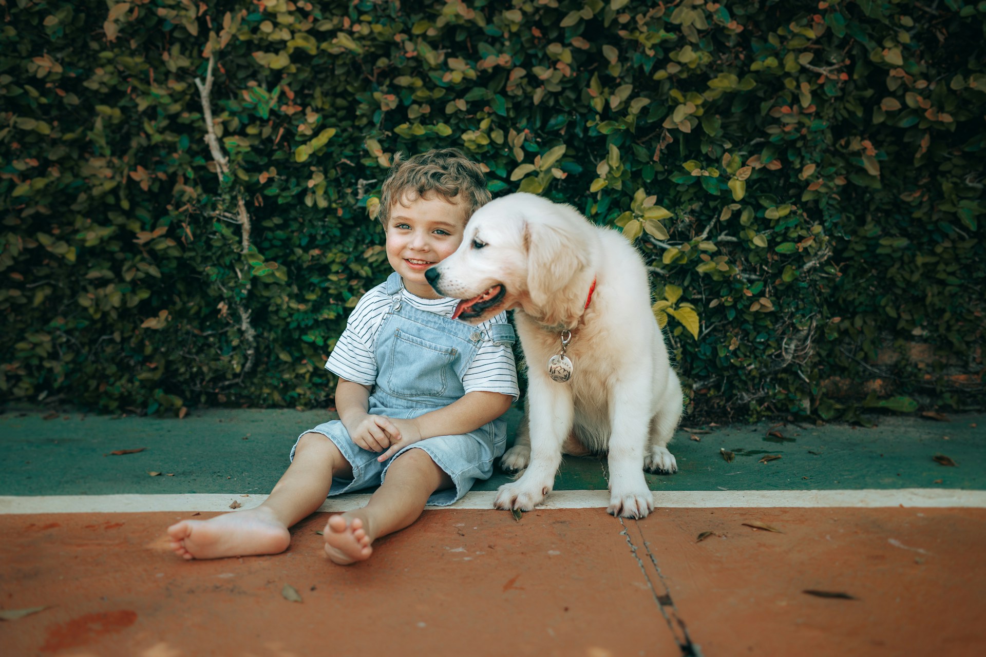 A smiling child sitting beside a golden retriever puppy on a sidewalk.