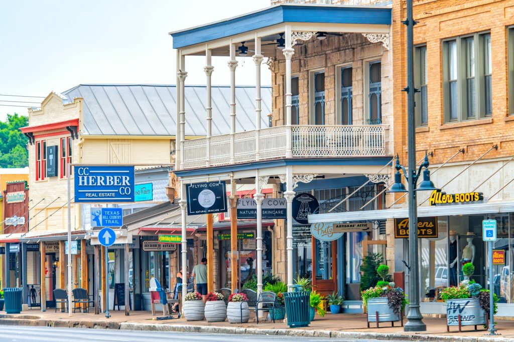 Colorful storefronts in a Texas Hill Country downtown area with signs and plants.