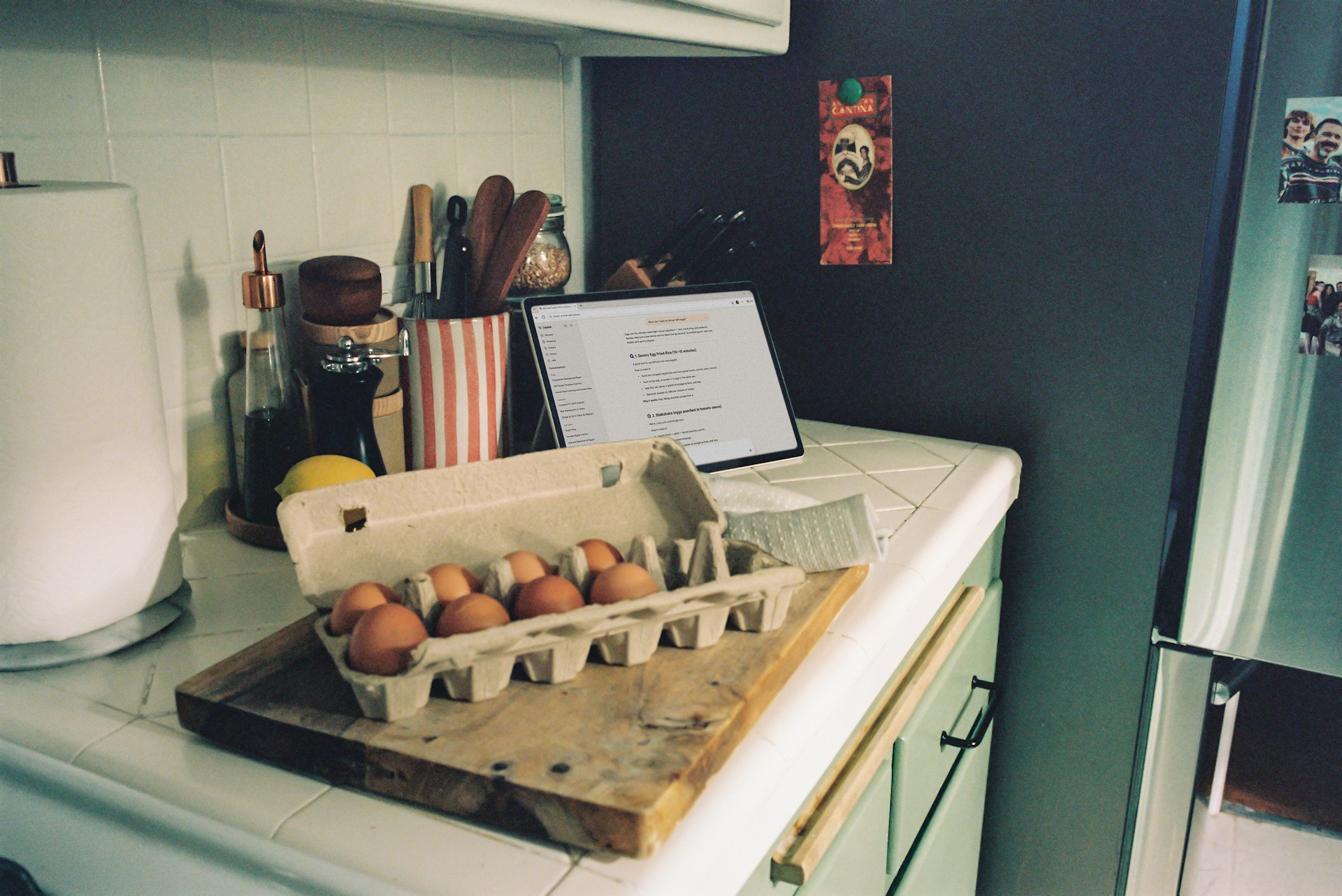 A kitchen counter featuring a carton of eggs, a laptop, and various cooking utensils.