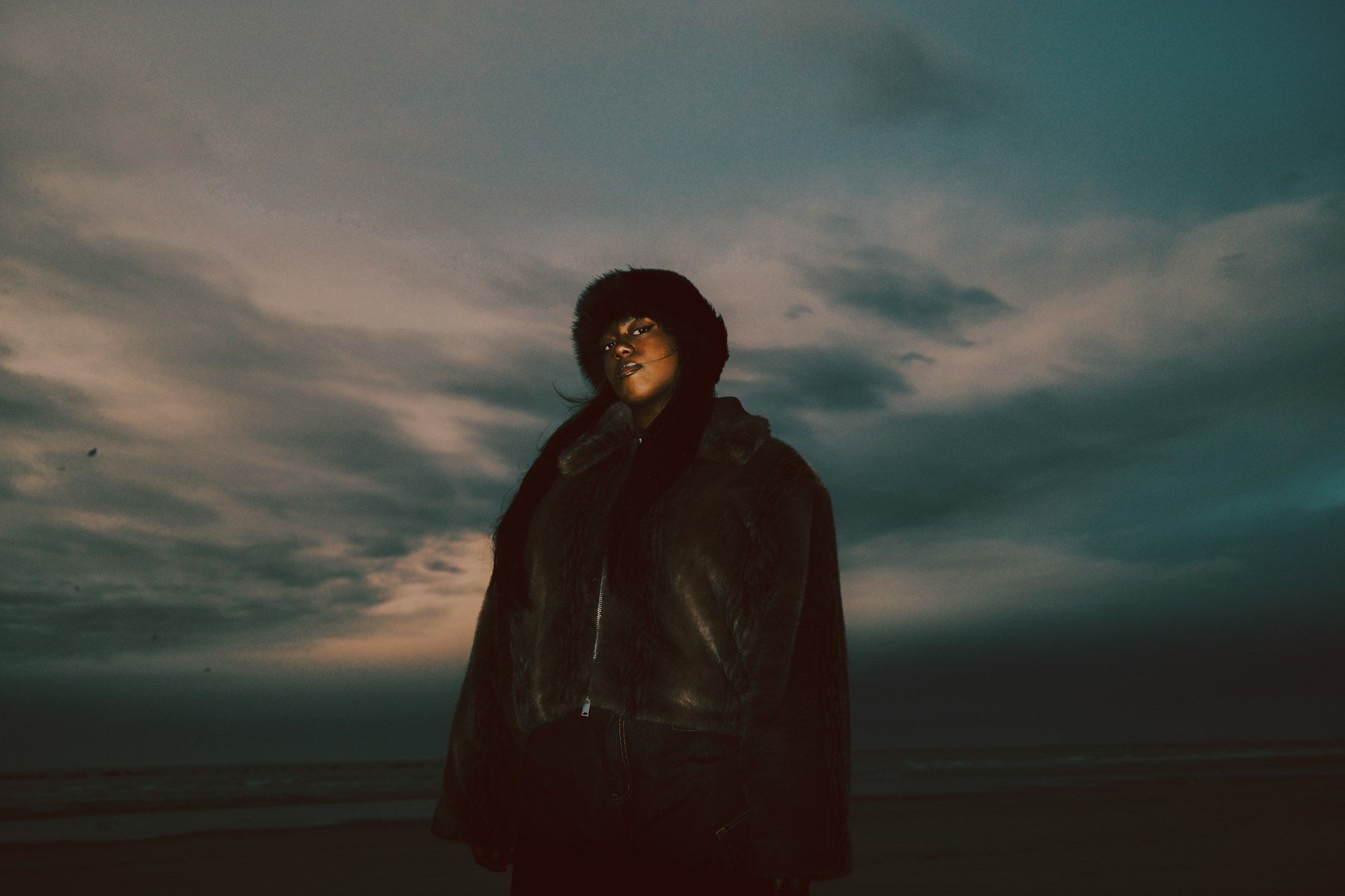 Woman in fur coat posing on the beach during twilight against moody skies