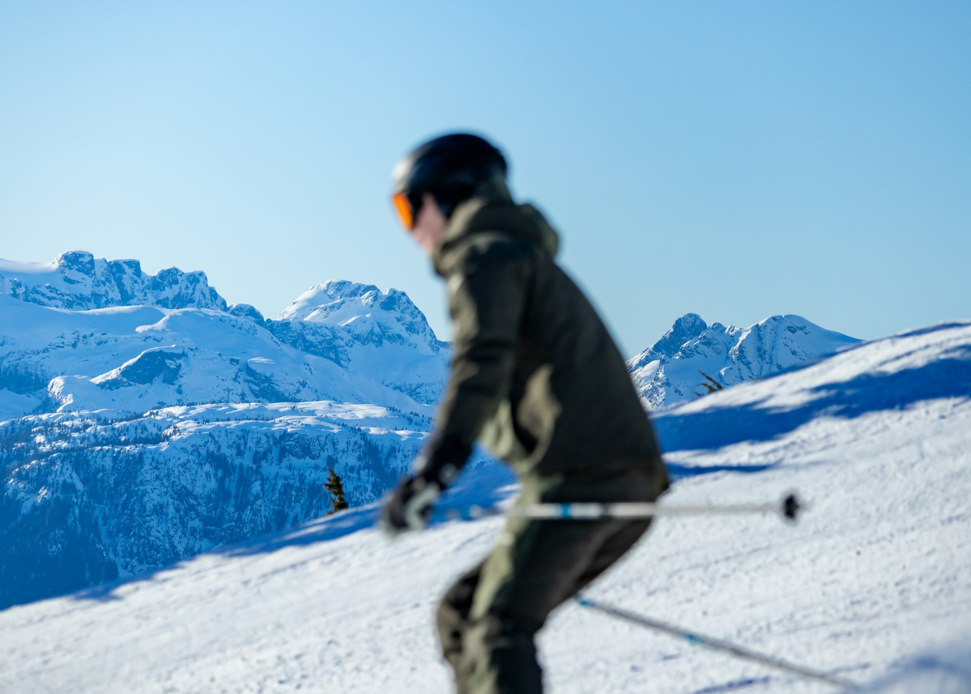 Skier in dark jacket descending snow-covered mountain slope with snowy peaks in background