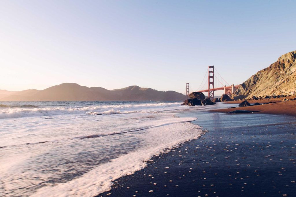 A picturesque view of the Golden Gate Bridge from the beach at sunset, with waves gently washing ashore.