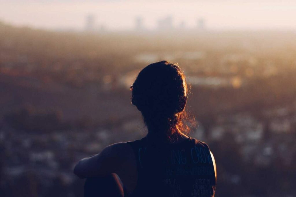 A person gazing at a distant cityscape during sunset.