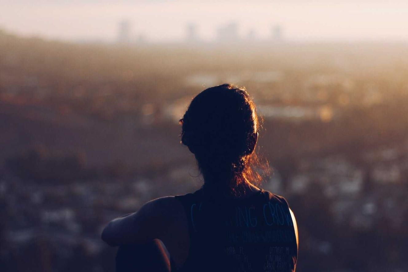 A person gazing at a distant cityscape during sunset.